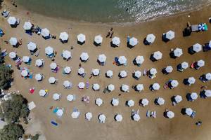 Urlaubsgäste auf Handtüchern und unter Sonnenschirmen am Monastiristrand in einer Bucht auf Paros