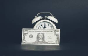US-Dollar Banknote vor weißem Wecker steht für Zeit ist Geld