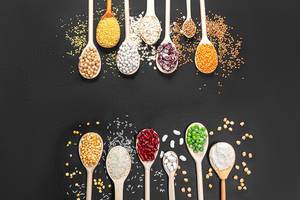 Various legumes, peas, buckwheat, rice, chickpeas, lentils, oat flakes, oat bran in wooden spoon on black background. Top view
