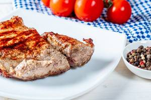 Veal steak on a white plate with spices and tomatoes