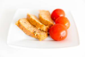 Vegan food: Mediterranean tofu Rosso by Taifun, next to three red tomatoes on a white plate