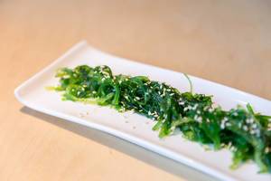 Vegan Japanese seaweed salad Goma Wakame with sesame seeds on a white longish plate
