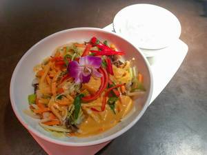 Vegan thai curry decorated with purple orchid flower in white bowl