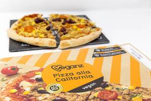 Vegane Holzofen-Pizza geviertelt auf Steinplatte vor Pizzakarton von Veganz