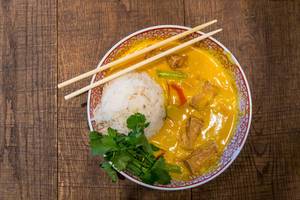 Veganes, asiatisches Essen im coa-Restaurant: Kokos-Curry mit Tofu, Paprika, Pilzen, Süßkartoffeln, Reis, Spinatblättern, in einer Schüssel mit Essstäbchen
