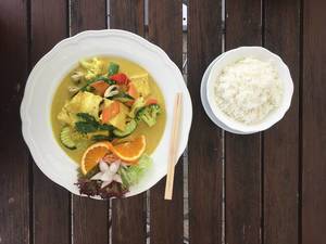 Veganes Essen mit Gemüse wie Brokkoli, Zucchini, Paprika und Blumenkohl, mit Tofu in fleischloser Curry-Kurkuma Soße, neben Essstäbchen und Reis