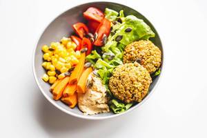 Veganes Gericht mit Falafel, Humus, Salat, Karotten, Tomaten, Mais und Sonnenblumenkernen