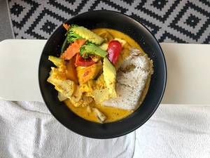 Veganes rotes Curry mit Reis und Gemüse in schwarzem Teller, Aufnahme von oben