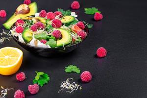 Vegetable salad with avocado, greens, onion micro-greens and raspberries on a black background (Flip 2020)