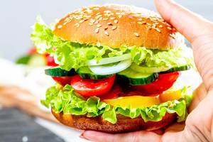 Vegetarian Burger with lettuce, cucumber, tomatoes, onions, bell pepper and sauce in a woman