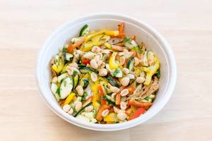Vegetarian meal with peppers, cucumbers, peanuts and herbs in white bowl