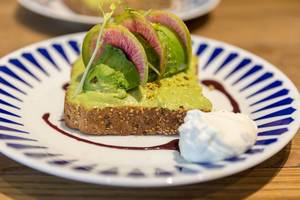 Vegetarian toast from whole wheat bread with guacamole, pistachio, yuzu & açai sauce, nutritional yeast and poached egg in close-up
