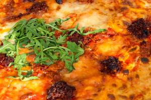 Vegetarische pikante Pizza NDUJA CALABRESE in der LOsteria, belegt mit Ruccola, Mozzarella, ital. Streichsalami und halb-getrockneten Kirschtomaten