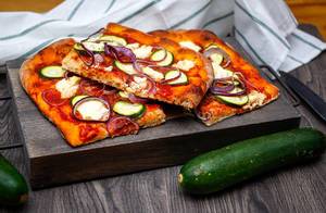 Vegetarische Pizza mit Zucchini und roten Zwiebeln auf einem Küchenbrett