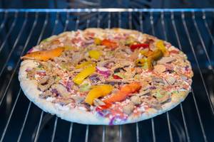 Vegetarische Protein Pizza mit Leinsamen, Quinoa und pulled Soybeans von Garden Gourmet ausgepackt gefroren auf einem Backblech im Ofen