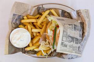 Vegetarischer Burger von Bus Burger in altem Vintage-Zeitungspapier gewickelt, mit Ziegenkäse-Patty, Senfsauce, cremigem Dip und Pommes Frites