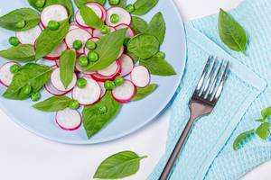 Vegetarischer Salat aus frischen Basilikumblättern, grüne Erbsen und Radieschen auf blauem Teller mit einer Gabel
