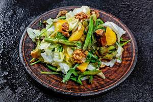 Vegetarischer Salat mit Spargel, Brokkoli, Pilzen, Rucola-Salat, Orangenstücke, Kerne und Nüsse, auf einem Holzteller auf einer schwarzen Abrbeitsfläche