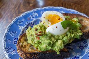 Vegetarisches Frühstück in den USA: Nahaufnahme von Mehrkornbrot-Toast mit Avocado, Ei, Chili und Limette auf blauem blumendekorierten Teller