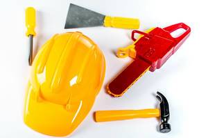 Verschiedene Bauarbeiter-Spielzeuge, wie ein gelber Helm, Hammer, Schraubenzieher, Spachten und eine Kettensäge