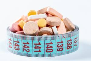 Verschiedene Diät-Pillen und Vitamintabletten zusammengehalten von Maßband vor weißem Hintergrund
