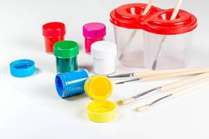 Verschiedene Farben in kleinen Behältern mit Pinseln und Wasserbehälter auf weißem Hintergrund