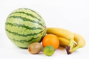 Verschiedene Früchte wie Wassermelone, Kiwi, Orange, Limette und Bananen, vor weißem Hintergrund