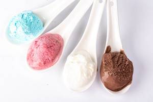 Verschiedene Sorten Eiscreme in bunten Farben, auf weißen Keramiklöffeln