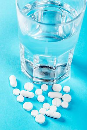 Verschiedene Tabletten und Medikamente neben gefülltem Wasserglas auf blauem Hintergrund