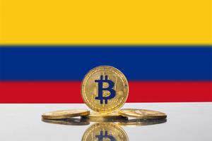 Vier Bitcoin-Münzen in gold vor der Flagge des südamerikanischen Landes Kolumbien