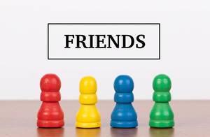 Vier farbige Spielfiguren auf Holztisch mit Text FRIENDS (Freunde) stehen für Freundschaft
