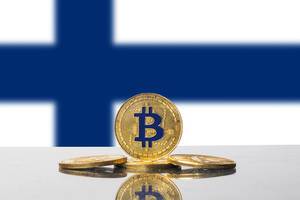 Vier glänzende goldene Bitcoins vor der weiß-blauen Flagge des nordeuropäischen Staates Finnland