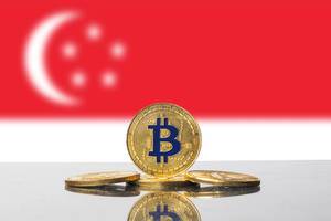 Vier goldene Bitcoin-Münzen vor der Flagge des südostasiatischen Stadtstaates Singapur