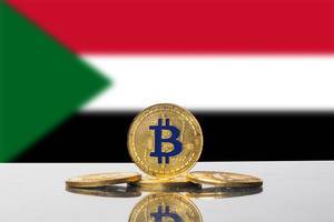 Vier goldene Bitcoins vor der Staatsflagge des Sudan