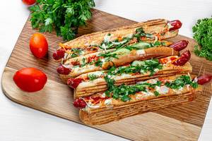 Vier Hot Dogs auf dem Küchenbrett mit frischen Kräutern und Tomaten