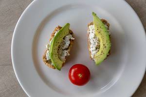 View from above of wholemeal bread rolls with cottage cheese and avocado with pepper and tomato on dish