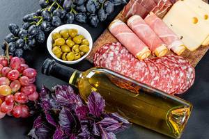 Voll Flasche Weißwein umgeben von Trauben, Oliven und einer Wurst- und Käseplatte auf schwarzem Hintergrund