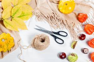 Vorbereitung für die Herbstferien: Schere, Zwirn, Kastanien, Kürbisse und bunte Blätter auf einem Holztisch