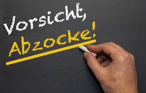 Vorsicht, Abzocke!: Weiße und gelbe Schrift auf Kreidetafel mit Hand in Ansatz - Nahaufnahme frontal