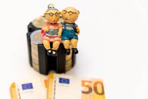 Vorsorge für das Alter - Gelscheine und Münzen umgeben ein Rentnerpaar symbolisch