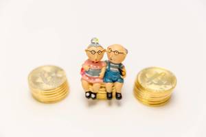 Vorsorgeplan für das Alter - Altes Paar sitzt auf Geldmünzen als Symbol for Altersvorsorge