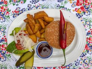 Wagyu-Burger mit Salat, Gurken, Zwiebeln, Tomaten, Chili-Paprika, Pommes frites und Barbecue Soße auf weißem Teller