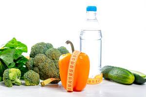 Wasserflasche und frisches Gemüse vor weißem Hintergrund mit Maßband - Konzept der Ernährung und Gesundheit - Lifestyle