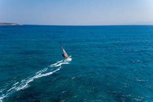 Wassersportler windsurft über die Wellen den blauen Mittelmeeres vor der griechischen Insel Paros