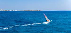 Water sports enthusiast windsurfing over the waves of the blue Mediterranean Sea in front of the Greek island of Paros