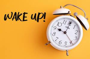 Wecker mit dem Text ‘Wake up!’ vor gelbem Hintergrund