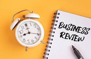 Wecker und ein Heft mit ‘Business review’ Text mit einem Filzstift drauf vor gelbem Hintergrund