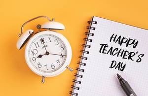 Wecker und ein Heft mit ‘Happy teacher’s day’ Text mit einem Filzstift drauf vor gelbem Hintergrund