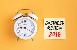 Wecker und ein Zettel mit ‘Business Review 2019’ Text vor gelbem Hintergrund