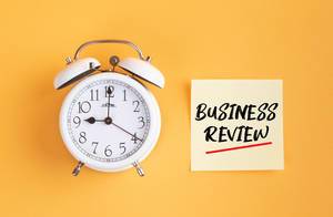 Wecker und ein Zettel mit ‘Business Review’ Text vor gelbem Hintergrund